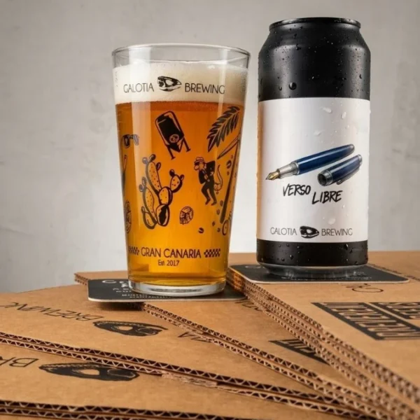Vaso y lata de cerveza "Verso Libre" de Galotia Brewing sobre cajas de cartón con logo de calavera.